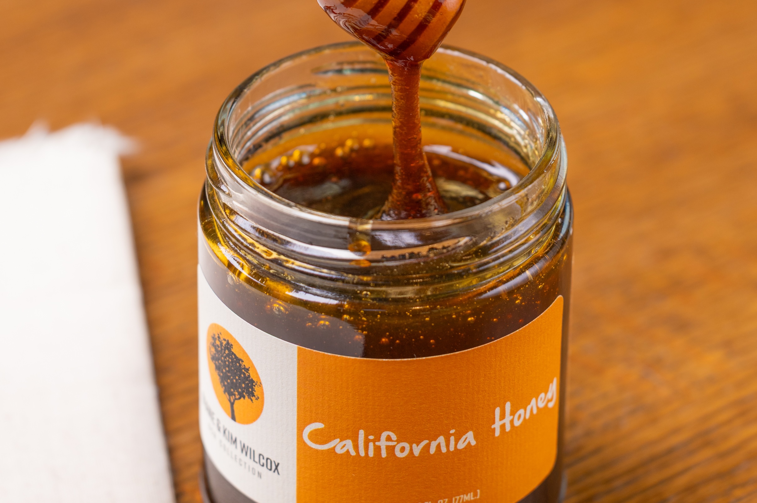 A hand using a honey stirrer to show the viscosity of the California Honey.